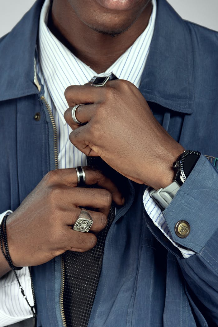 Close-up of a man adjusting his tie adorned with stylish rings and watch.